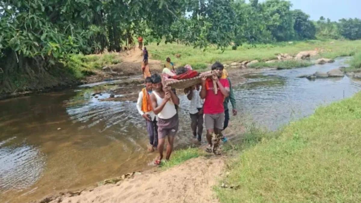 चतरा के कुंदा में दो मुहायन नदी पर पुल न होने से मरीज को खाट पर उठाकर मुख्य सड़क तक ले जाते ग्रामीण।